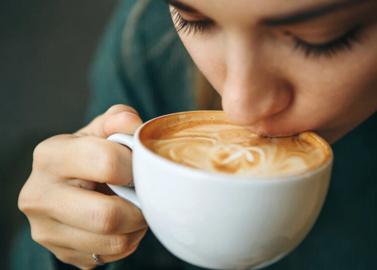 Close up girl is drinking coffee. She enjoys her morning cappuccino or flat white.