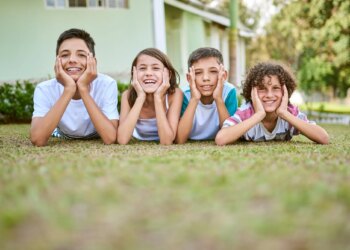 Portrait of a group of happy siblings lying together on the grass in their backyard.