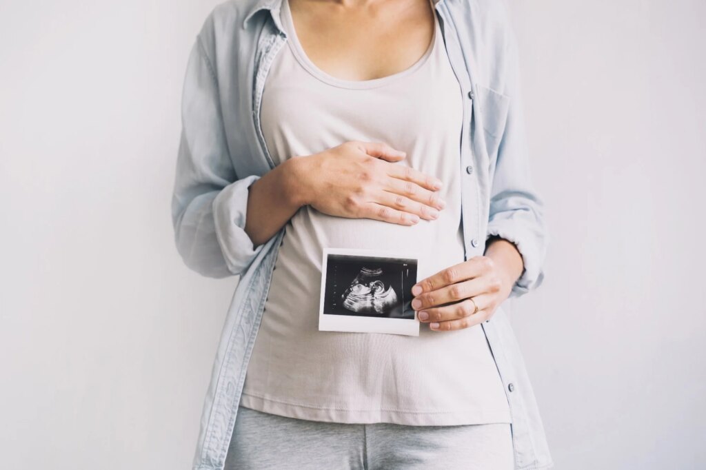 Pregnant woman holding ultrasound baby image. Close-up of pregnant belly and sonogram photo in hands of mother.