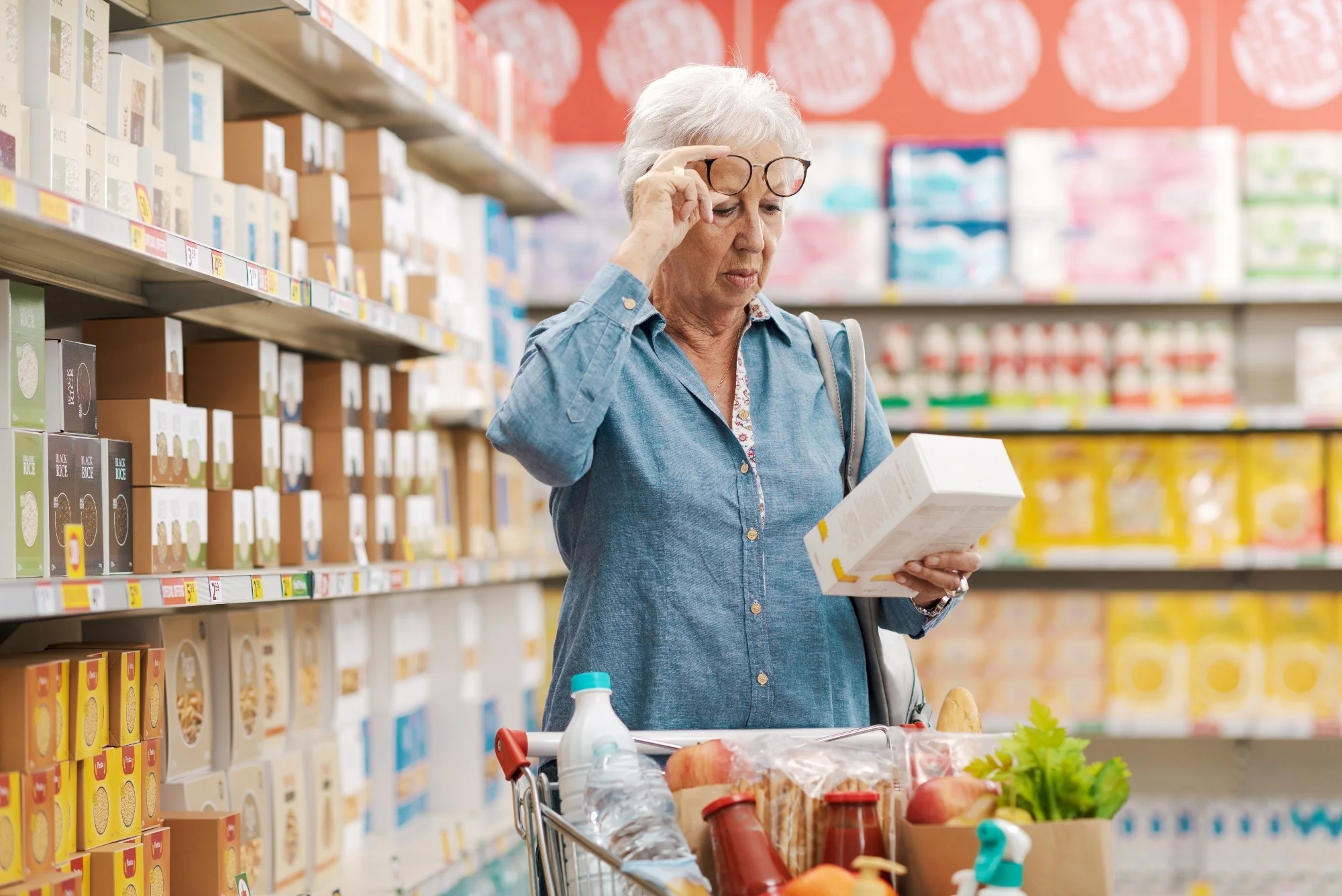 Older woman unable to read the text on a product package in supermarket and she is adjusting her glasses