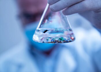 Scientist examining small plastic particles suspended in water in a laboratory flask