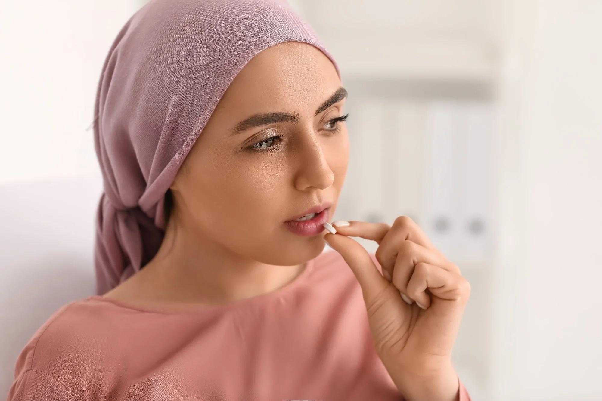 Young woman after chemotherapy taking pill in clinic, closeup