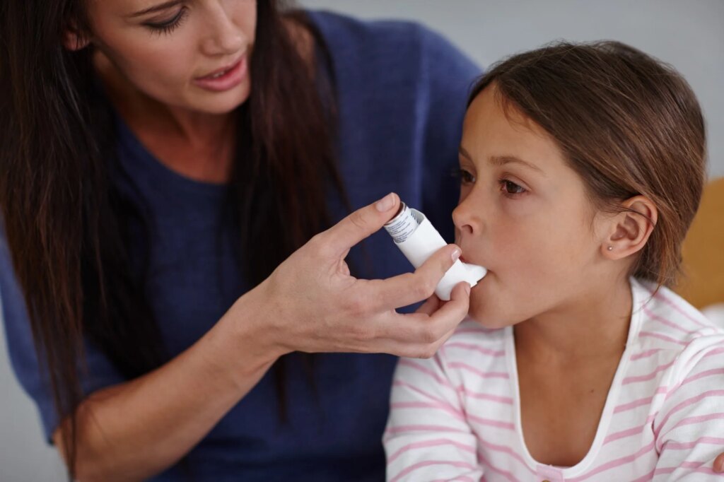 hot of a caring mother giving her daughter an asthma pump at home.