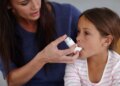 hot of a caring mother giving her daughter an asthma pump at home.