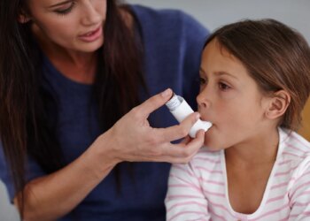 hot of a caring mother giving her daughter an asthma pump at home.