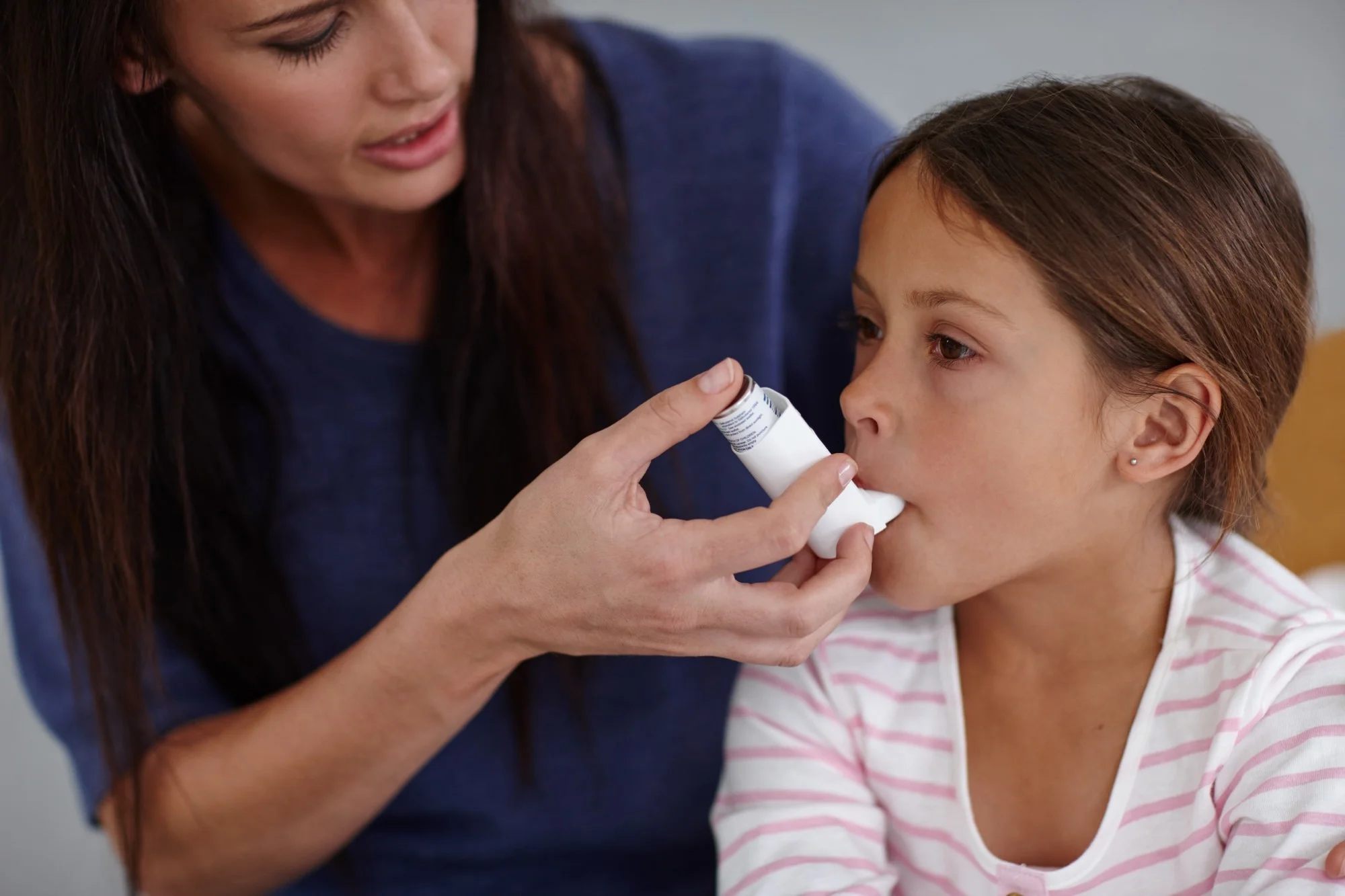 hot of a caring mother giving her daughter an asthma pump at home.