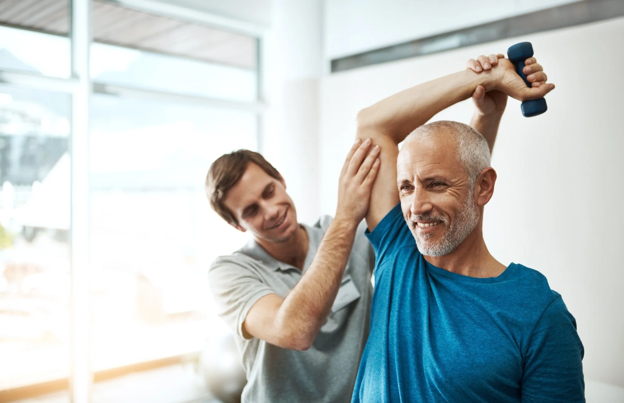Strength, physiotherapist and mature man with dumbbell in clinic for physical therapy,