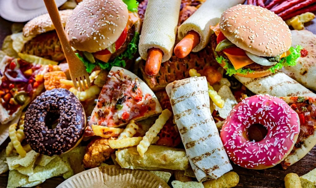 Assortment of ultraprocessed foods, including burgers, hot dogs, pizza, fries, and colorful doughnuts.